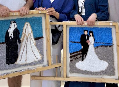 Dos cuadros de tufting con escenas de boda, sostenidos delante de la pared de lanas